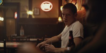 Movie still from “The Greatest Beer Run Ever” (2022), directed by Peter Farrelly – A man sitting at a table holding a glass of beer; Medium shot, Over the shoulder angle