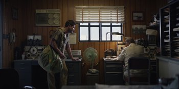 Movie still from “The Greatest Beer Run Ever” (2022), directed by Peter Farrelly – A man standing in front of two other men in an office; Wide shot, Low angle