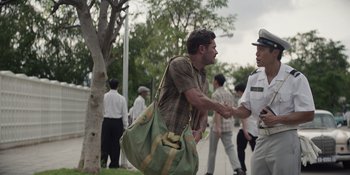 Movie still from “The Greatest Beer Run Ever” (2022), directed by Peter Farrelly – A man shaking hands with a police officer in a crowd; Wide shot, Over the shoulder angle
