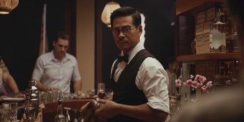 Movie still from “The Greatest Beer Run Ever” (2022), directed by Peter Farrelly – A man in a black vest and white shirt holding a glass; Medium shot, Over the shoulder angle