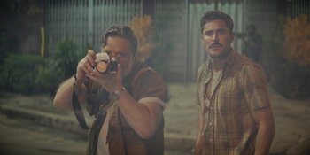Movie still from “The Greatest Beer Run Ever” (2022), directed by Peter Farrelly – A man taking a picture of another man with a camera; Medium shot, Over the shoulder angle