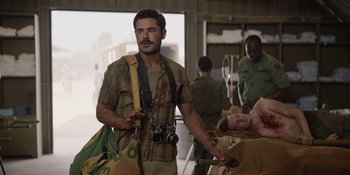 Movie still from “The Greatest Beer Run Ever” (2022), directed by Peter Farrelly – A man holding a camera while standing next to other people; Medium shot, Over the shoulder angle