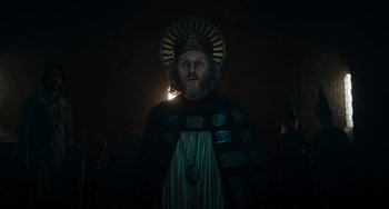 Movie still from “The Green Knight” (2021), directed by David Lowery – A man with a beard wearing a crown and a robe; Medium shot, Low angle
