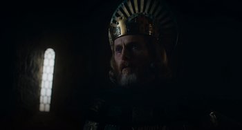 Movie still from “The Green Knight” (2021), directed by David Lowery – A man with a beard wearing a gold crown; Close Up shot, Low angle