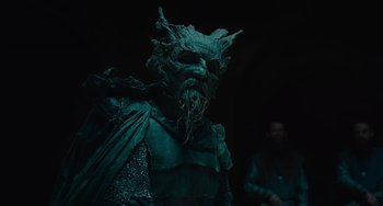 Movie still from “The Green Knight” (2021), directed by David Lowery – A man with a beard and a green mask; Medium shot, Over the shoulder angle
