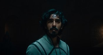 Movie still from “The Green Knight” (2021), directed by David Lowery – A man with long black hair and a beard is looking at the camera; Close Up shot, Low angle