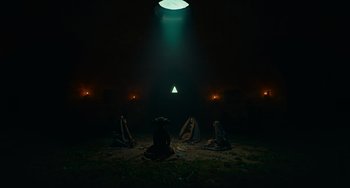 Movie still from “The Green Knight” (2021), directed by David Lowery – A group of people sitting on the ground under a light; Extreme Wide shot, Low angle