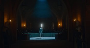 Movie still from “The Green Knight” (2021), directed by David Lowery – A man standing in a room with a light shining on him; Extreme Wide shot, Low angle