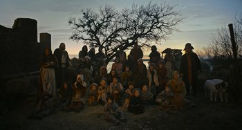 Movie still from “The Green Knight” (2021), directed by David Lowery – A group of people gathered under a large tree; Wide shot, High angle
