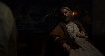 Movie still from “The Green Knight” (2021), directed by David Lowery – A man with a long beard sitting in a chair; Medium shot, Over the shoulder angle