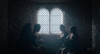 Movie still from “The Green Knight” (2021), directed by David Lowery – A group of people sitting in front of a window; Wide shot, Low angle