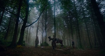 Movie still from “The Green Knight” (2021), directed by David Lowery – A group of people standing in the middle of a forest; Extreme Wide shot, Low angle