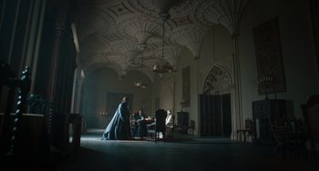 Movie still from “The Green Knight” (2021), directed by David Lowery – Two men sitting in a large room with a chandelier overhead; Extreme Wide shot, Low angle
