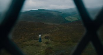 Movie still from “The Green Knight” (2021), directed by David Lowery – A woman standing on top of a green hillside; Extreme Wide shot, High angle