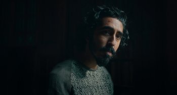 Movie still from “The Green Knight” (2021), directed by David Lowery – A man with long hair and a beard is looking at the camera; Close Up shot, Low angle