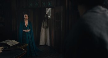 Movie still from “The Green Knight” (2021), directed by David Lowery – A woman standing in front of a doorway in a room; Wide shot, Over the shoulder angle