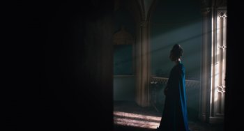 Movie still from “The Green Knight” (2021), directed by David Lowery – A woman in a blue dress standing in a room; Wide shot, Over the shoulder angle