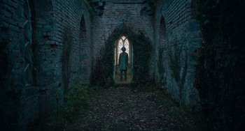 Movie still from “The Green Knight” (2021), directed by David Lowery – A man standing in a tunnel with a window in the background; Extreme Wide shot, Low angle