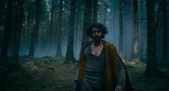 Movie still from “The Green Knight” (2021), directed by David Lowery – A man with a beard is walking through the woods; Medium shot, Low angle