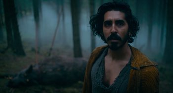 Movie still from “The Green Knight” (2021), directed by David Lowery – A man with long hair and a beard standing in the woods; Medium shot, Low angle