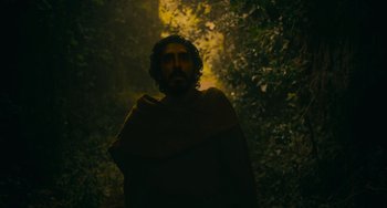 Movie still from “The Green Knight” (2021), directed by David Lowery – A man with a beard wearing a robe in the woods; Medium shot, Low angle