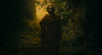 Movie still from “The Green Knight” (2021), directed by David Lowery – A man standing in the middle of a forest; Wide shot, Low angle