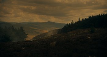 Movie still from “The Green Knight” (2021), directed by David Lowery – A view of a mountain range with trees in the foreground; Extreme Wide shot, Low angle