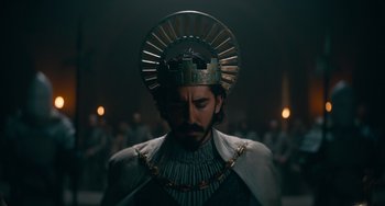 Movie still from “The Green Knight” (2021), directed by David Lowery – A man wearing a crown and a chain around his neck; Medium shot, Low angle