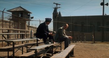 Movie still from “The Green Mile” (1999), directed by Frank Darabont – Two men sitting on picnic benches on a field; Wide shot, High angle