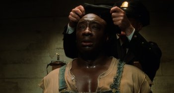 Movie still from “The Green Mile” (1999), directed by Frank Darabont – A man putting on a black hat while a man in a black suit holds a black hat; Close Up shot, High angle