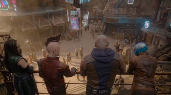 Movie still from “The Guardians of the Galaxy Holiday Special” (2022), directed by James Gunn – Two people standing on a balcony looking at a crowd of people; Wide shot, Over the shoulder angle