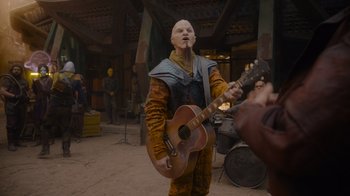 Movie still from “The Guardians of the Galaxy Holiday Special” (2022), directed by James Gunn – A person in a costume playing a guitar in front of a crowd; Medium shot, Over the shoulder angle