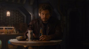 Movie still from “The Guardians of the Galaxy Holiday Special” (2022), directed by James Gunn – A man sitting at a table with a drink in front of him; Medium shot, Over the shoulder angle