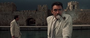 Movie still from “The Guns of Navarone” (1961), directed by J. Lee Thompson – A man smoking a cigarette while standing in front of a castle; Medium shot, Low angle