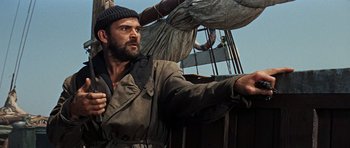 Movie still from “The Guns of Navarone” (1961), directed by J. Lee Thompson – A man standing on top of a boat in the water; Medium shot, Low angle