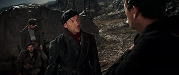 Movie still from “The Guns of Navarone” (1961), directed by J. Lee Thompson – A man in a black coat and hat talking to another man in a black hat; Medium shot, Over the shoulder angle