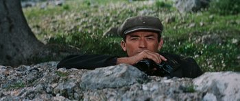 Movie still from “The Guns of Navarone” (1961), directed by J. Lee Thompson – A man wearing a hat is leaning against a rock; Close Up shot, Low angle