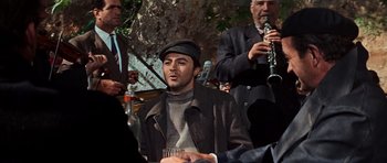 Movie still from “The Guns of Navarone” (1961), directed by J. Lee Thompson – A group of men playing music in a park; Medium shot, Over the shoulder angle