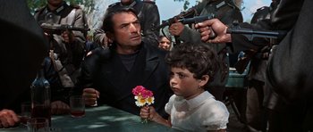 Movie still from “The Guns of Navarone” (1961), directed by J. Lee Thompson – A man and a child holding flowers and guns; Medium shot, High angle