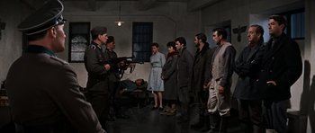 Movie still from “The Guns of Navarone” (1961), directed by J. Lee Thompson – A group of people standing in a room with a gun; Wide shot, High angle