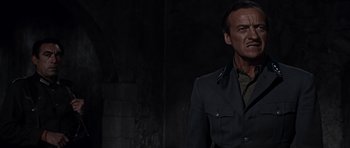 Movie still from “The Guns of Navarone” (1961), directed by J. Lee Thompson – A man in a military uniform standing in a dark room; Medium shot, Low angle