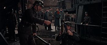 Movie still from “The Guns of Navarone” (1961), directed by J. Lee Thompson – A group of men in uniforms are standing in front of a group of people; Medium shot, High angle