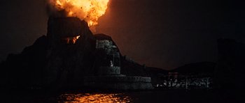 Movie still from “The Guns of Navarone” (1961), directed by J. Lee Thompson – A fire is burning in the sky near a castle; Extreme Wide shot, Low angle