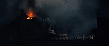 Movie still from “The Guns of Navarone” (1961), directed by J. Lee Thompson – A fire is burning in the sky near a building; Extreme Wide shot, Low angle