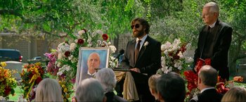 Movie still from “The Hangover Part III” (2013), directed by Todd Phillips – A man in a suit and tie standing next to a picture; Wide shot, Over the shoulder angle