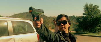 Movie still from “The Hangover Part III” (2013), directed by Todd Phillips – A man holding a gun in front of a white car; Medium shot, Over the shoulder angle