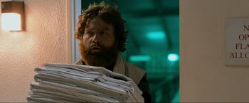 Movie still from “The Hangover Part III” (2013), directed by Todd Phillips – A man with a beard holding a stack of folded sheets; Medium shot, Over the shoulder angle
