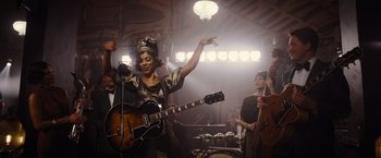 Movie still from “Death on the Nile” (2022), directed by Kenneth Branagh – A group of people that are standing up with a guitar; Medium shot, Low angle