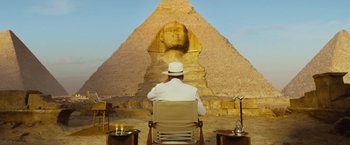 Movie still from “Death on the Nile” (2022), directed by Kenneth Branagh – A man sitting in front of an egyptian pyramid; Wide shot, Low angle