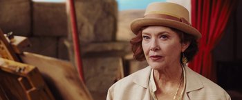 Movie still from “Death on the Nile” (2022), directed by Kenneth Branagh – An older woman wearing a tan hat and a beige jacket; Close Up shot, Over the shoulder angle